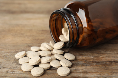 Photo of Bottle with vitamin pills on wooden table, closeup