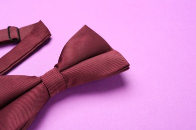 Photo of Stylish burgundy bow tie on violet background, closeup. Space for text