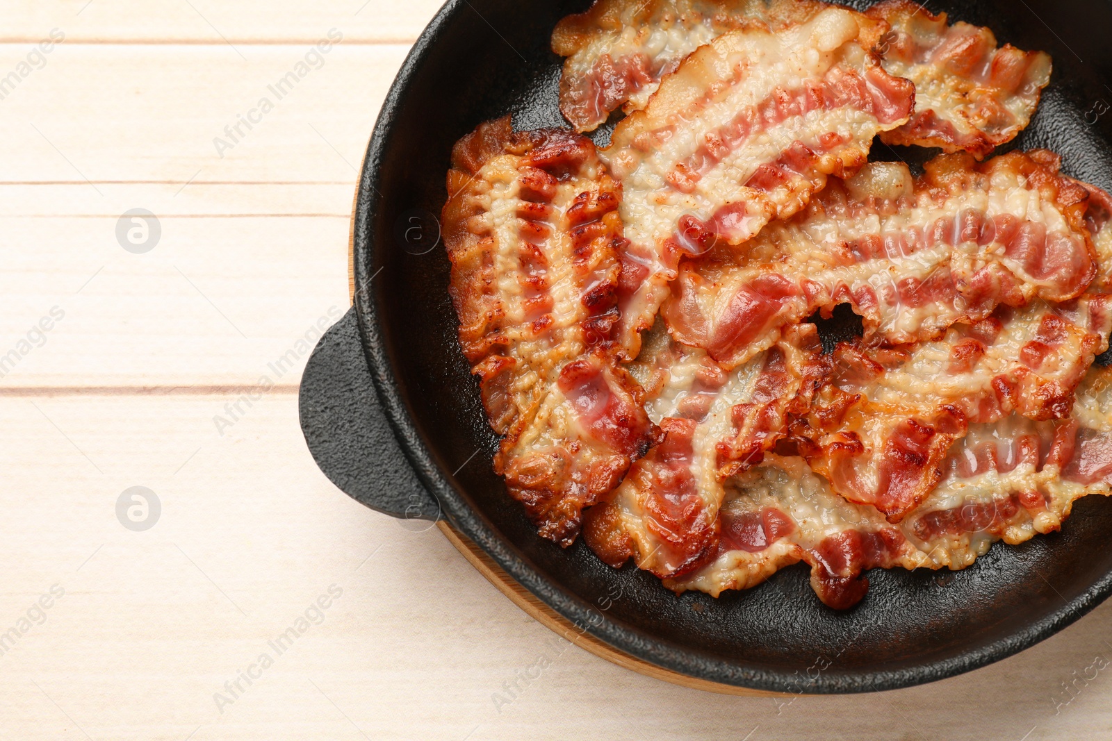 Photo of Delicious bacon slices in frying pan on white wooden table, top view. Space for text