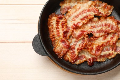 Delicious bacon slices in frying pan on white wooden table, top view. Space for text