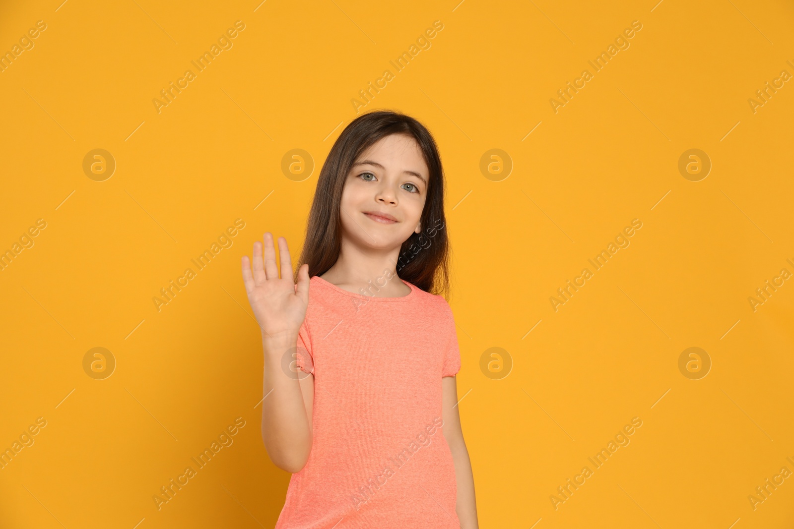 Photo of Happy little girl waving to say hello on yellow background