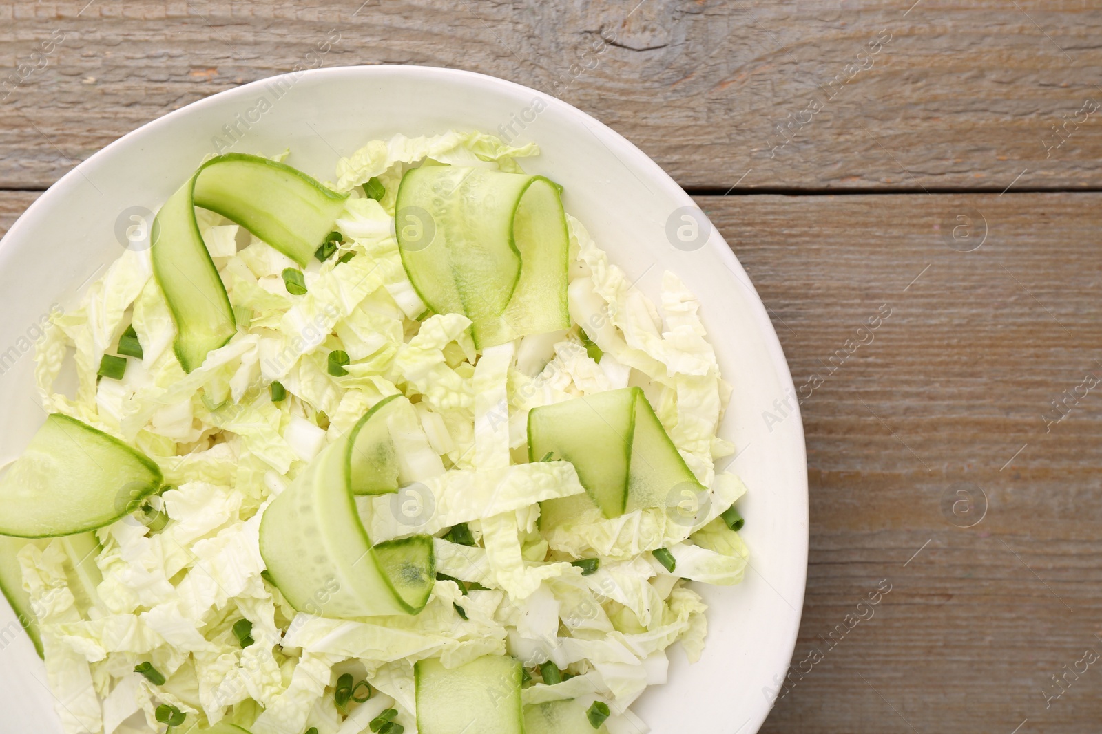 Photo of Tasty salad with Chinese cabbage, cucumber and green onion in bowl on wooden table, top view