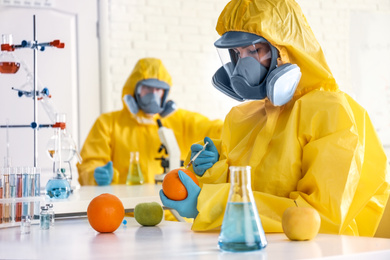 Photo of Scientist in chemical protective suit injecting orange at laboratory