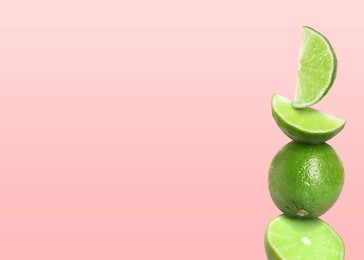 Image of Stacked whole and cut limes on light pale pink background, space for text