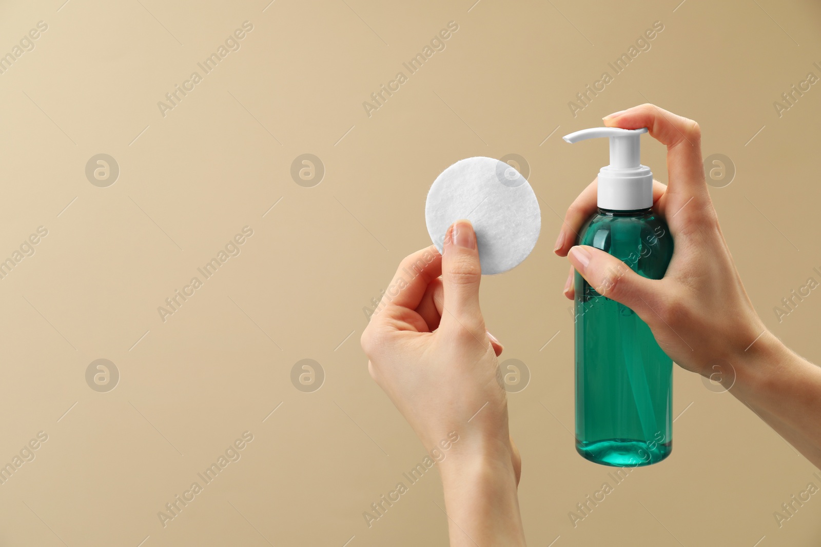 Photo of Woman applying makeup remover onto cotton pad on beige background, closeup. Space for text