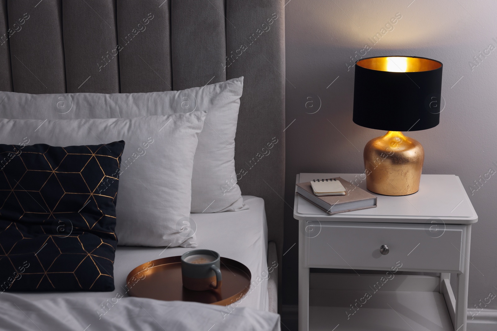 Photo of Stylish lamp and book on bedside table indoors. Bedroom interior element