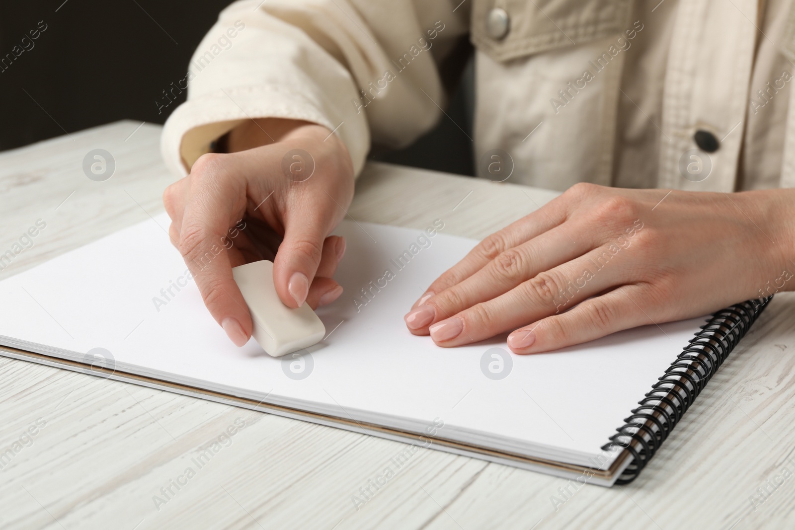 Photo of Woman erasing something in notebook at white wooden table, closeup