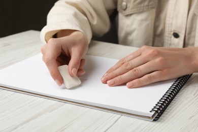 Photo of Woman erasing something in notebook at white wooden table, closeup