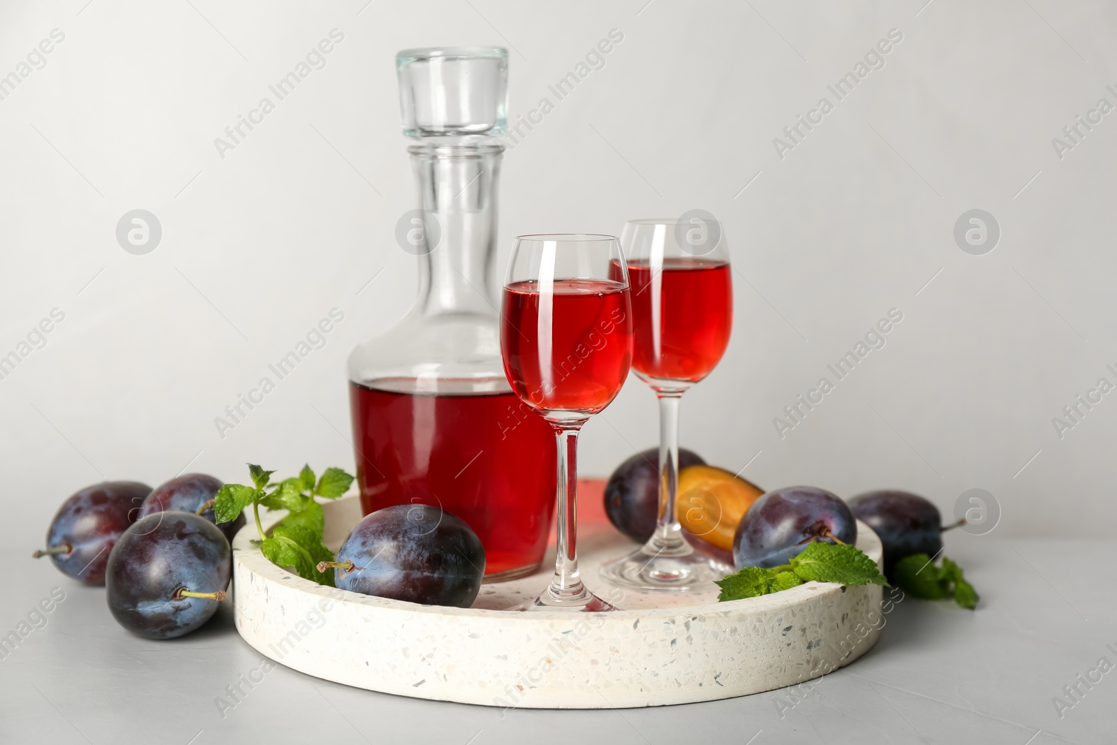 Photo of Delicious plum liquor, mint and ripe fruits on light table. Homemade strong alcoholic beverage