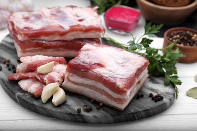 Pieces of tasty pork fatback with garlic and peppercorns on white wooden table, closeup