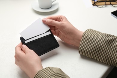 Photo of Woman holding leather business card holder with blank card at white table, closeup