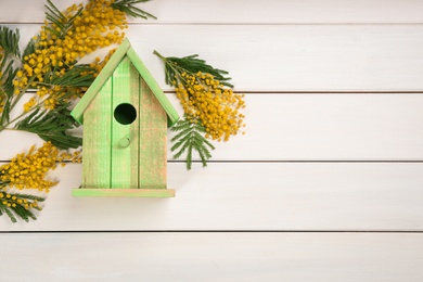 Photo of Stylish bird house and fresh mimosas on white wooden background, flat lay. Space for text