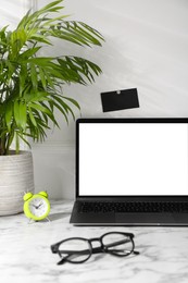 Photo of Office workplace with computer, glasses, houseplant and stationery on marble table near white wall