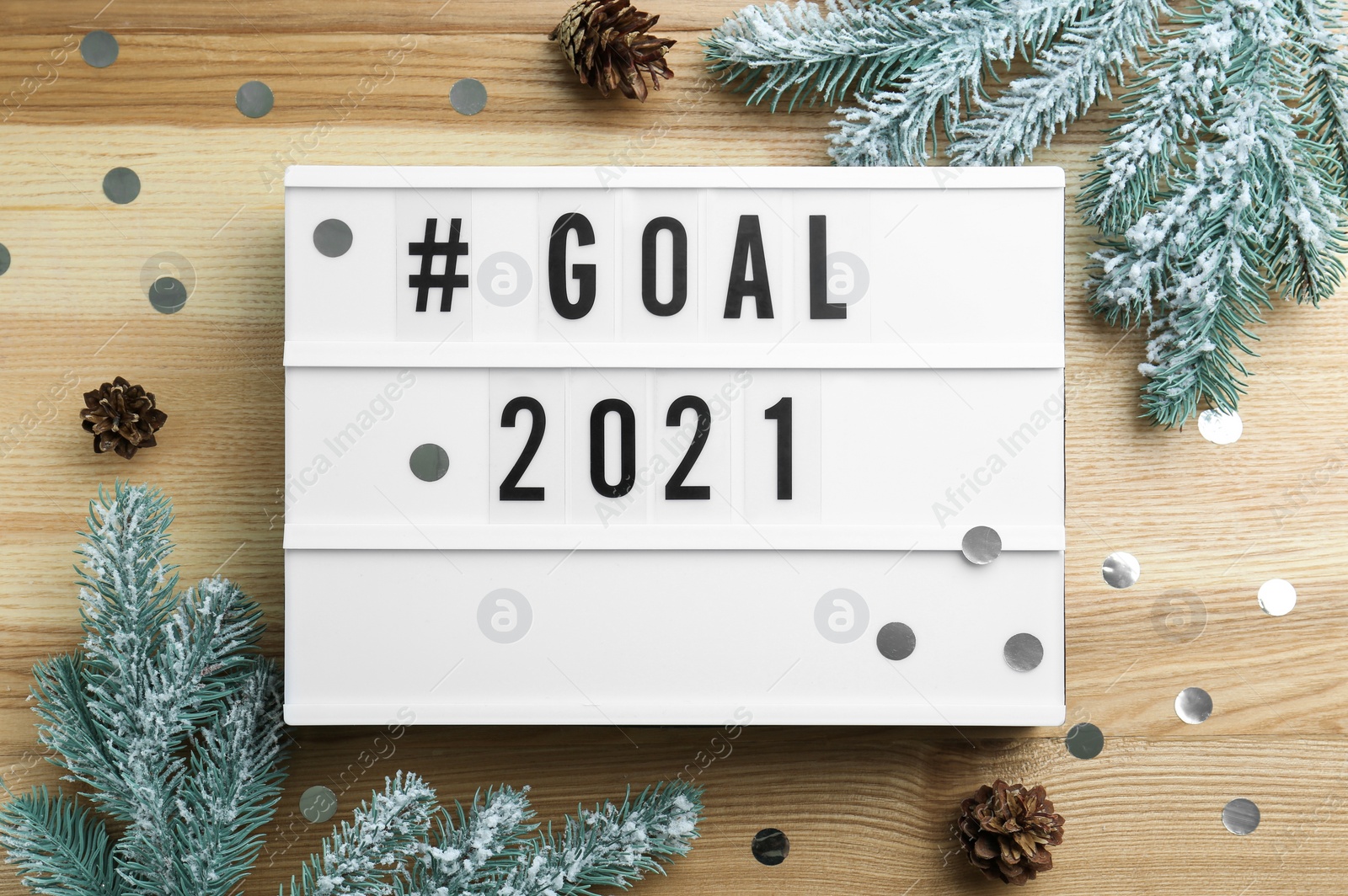 Photo of Light box with hashtag Goal 2021 near fir branches and cones on wooden table, flat lay. New year targets