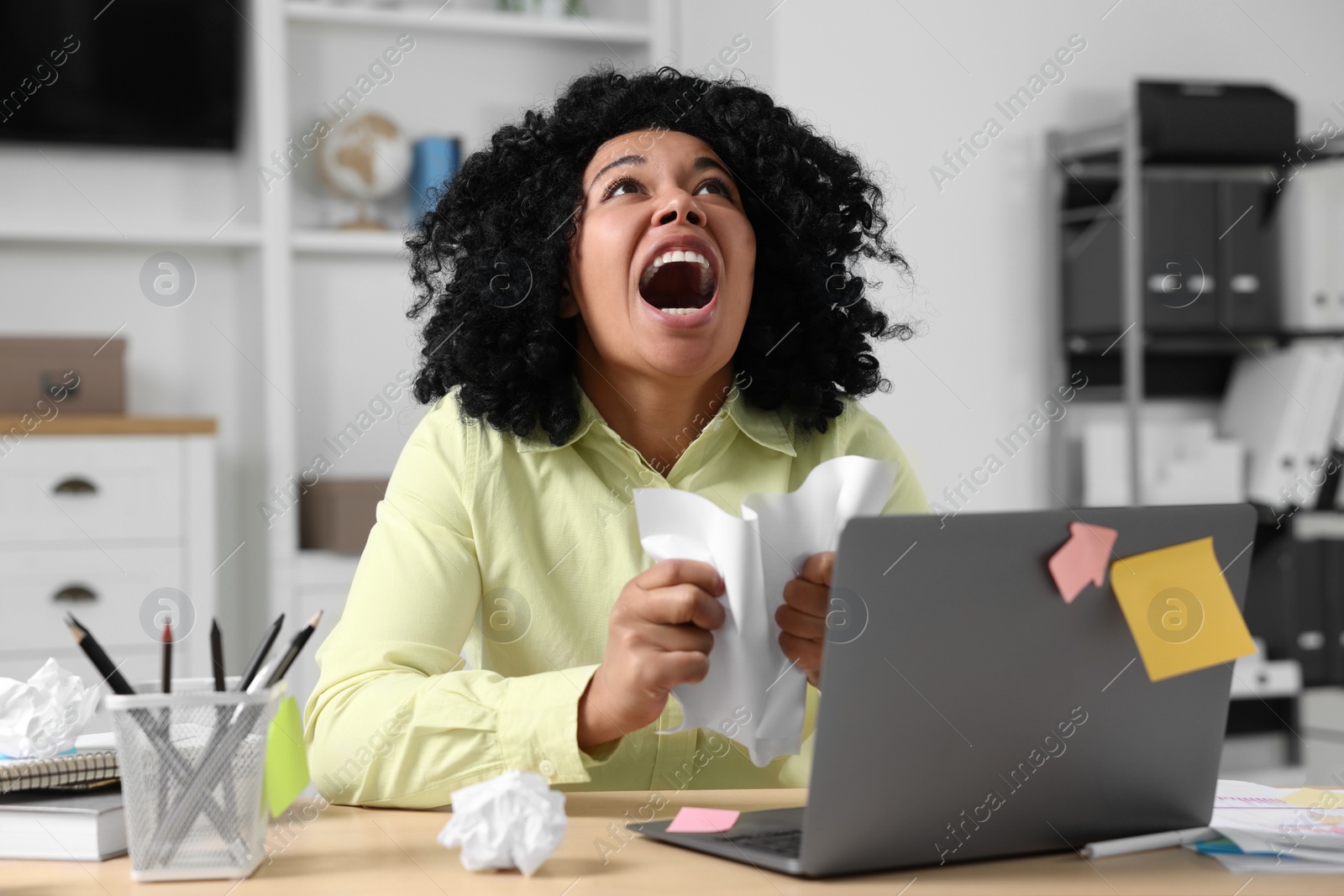 Photo of Stressful deadline. Emotional woman shouting and crumpling document at wooden table in office