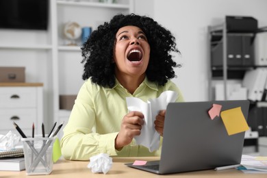 Stressful deadline. Emotional woman shouting and crumpling document at wooden table in office
