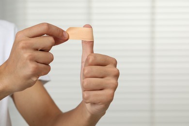 Man putting sticking plaster onto thumb indoors, closeup