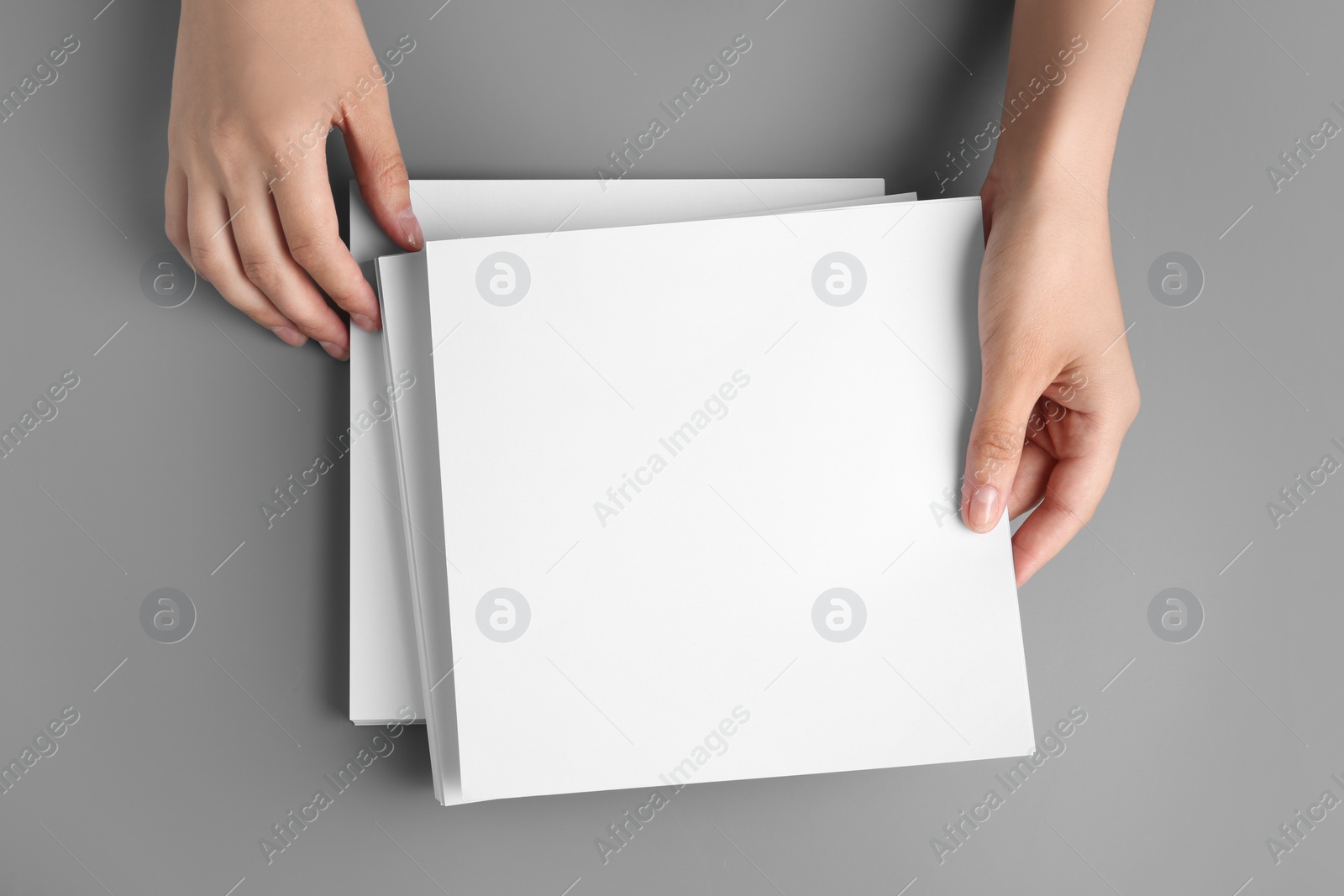 Photo of Woman holding blank paper sheets for brochure at grey table, top view. Mock up