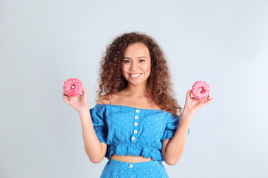 Beautiful African-American woman with donuts on light grey background