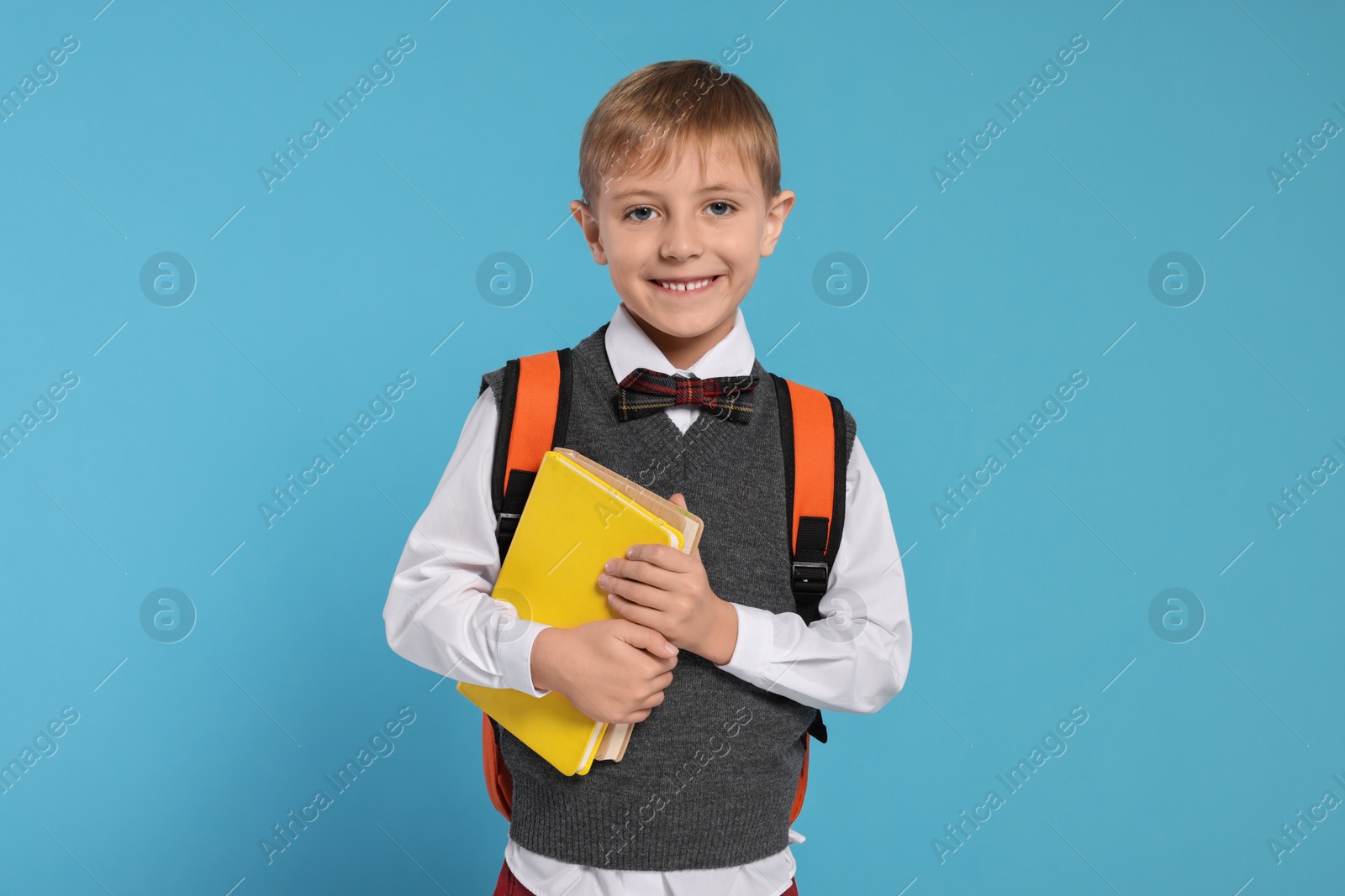 Photo of Happy schoolboy with backpack and books on light blue background