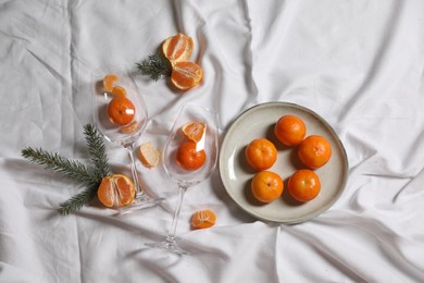 Photo of Delicious fresh ripe tangerines and glasses on white bedsheet, flat lay