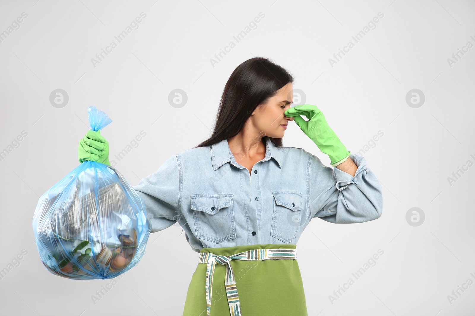 Photo of Woman holding full garbage bag on light background