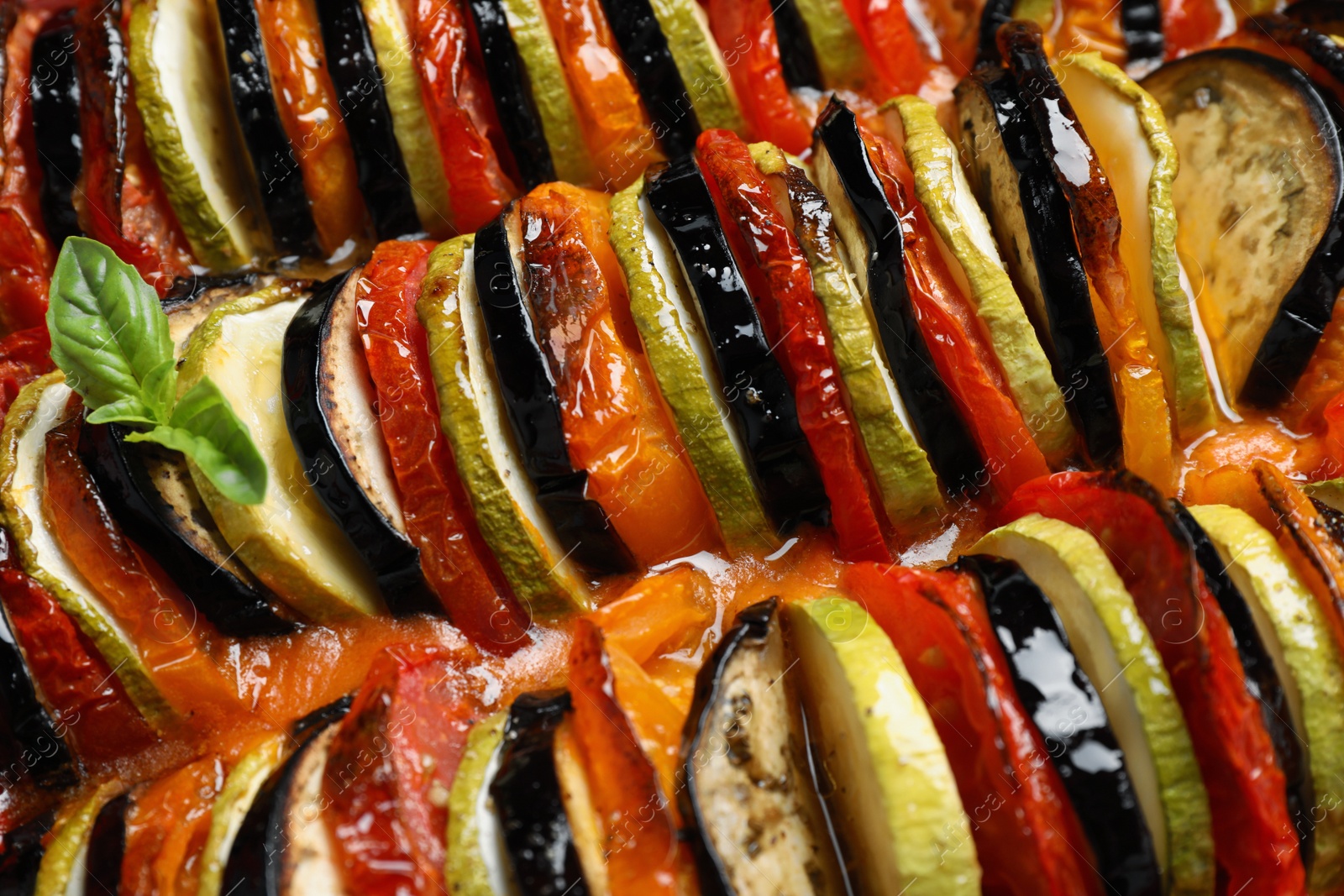 Photo of Delicious homemade ratatouille with basil as background, closeup