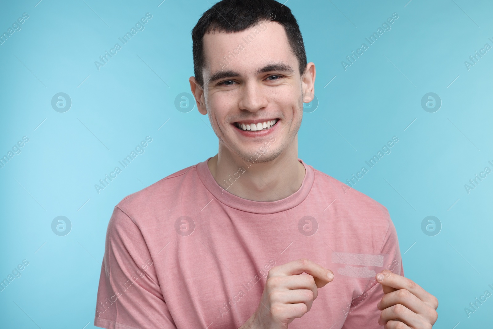 Photo of Young man with whitening strips on light blue background