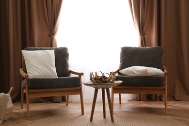 Photo of Comfortable armchairs near window with stylish curtains in living room. Interior design