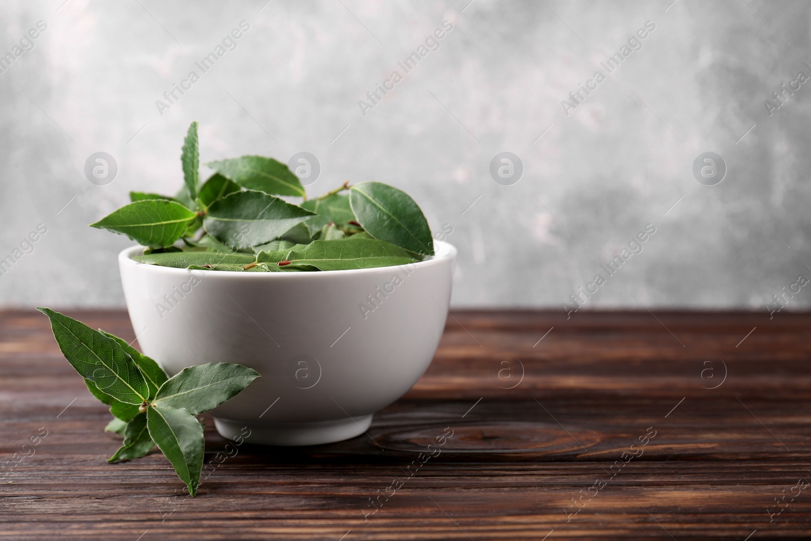 Photo of Fresh green bay leaves in bowl on wooden table, closeup. Space for text