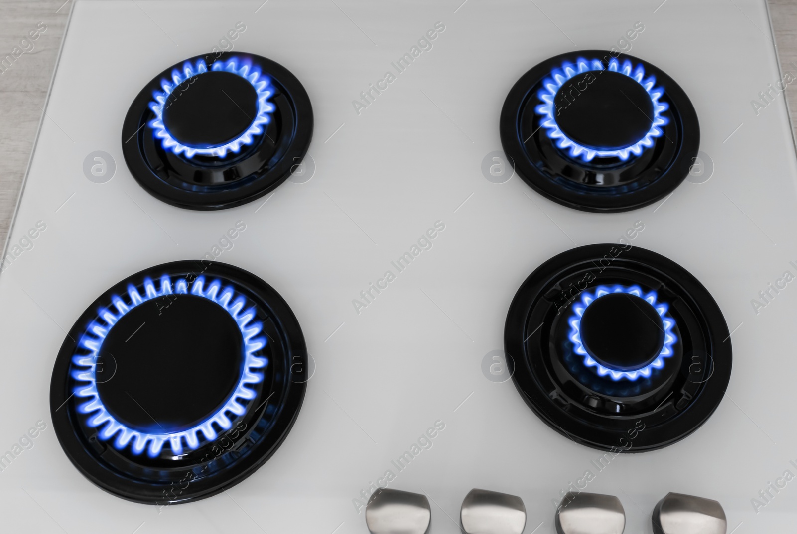 Photo of Modern gas cooktop with burning blue flames in kitchen