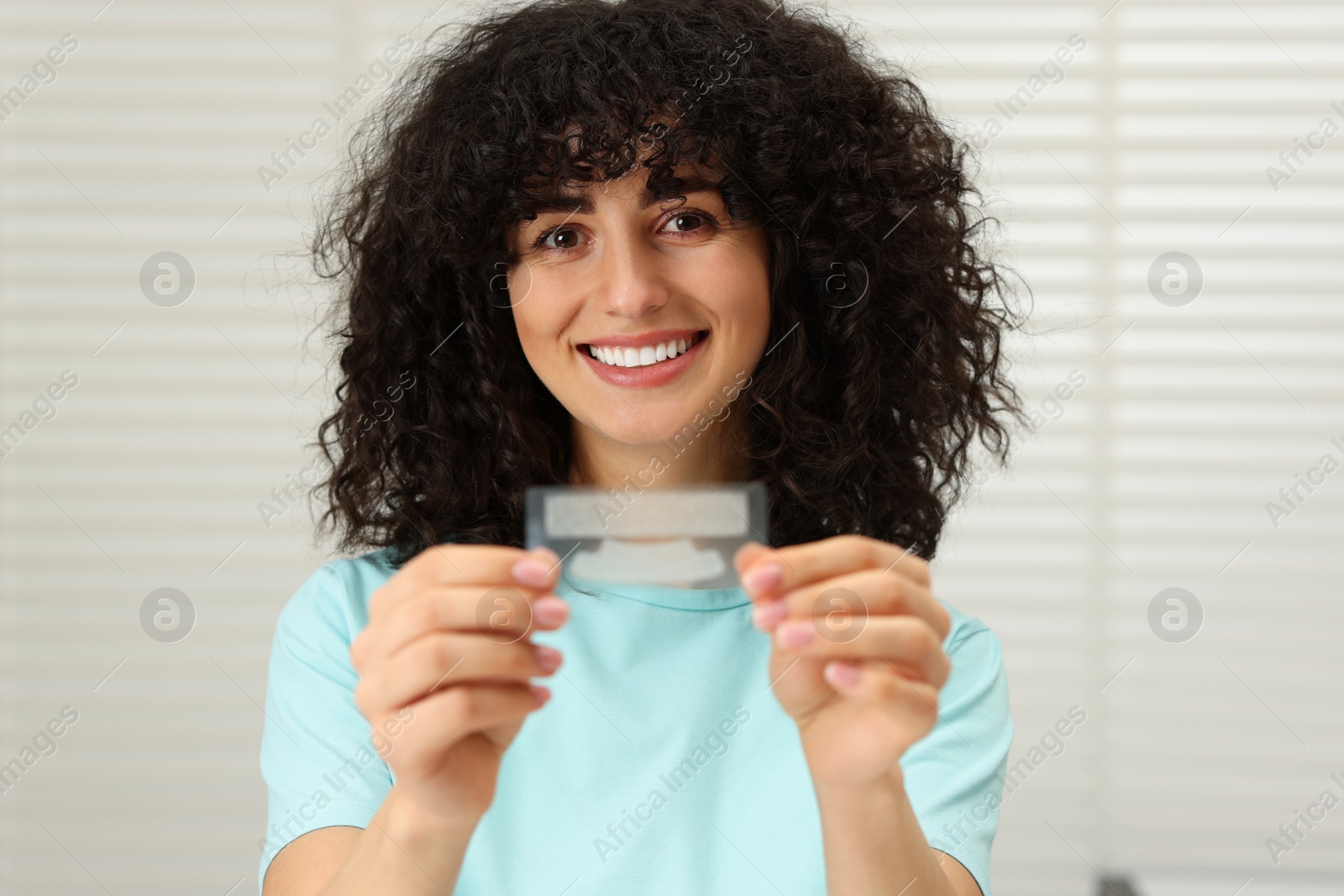 Photo of Young woman holding teeth whitening strips indoors