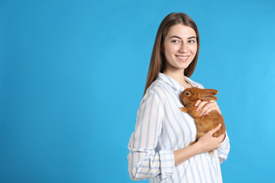 Photo of Young woman with adorable rabbit on blue background, space for text. Lovely pet