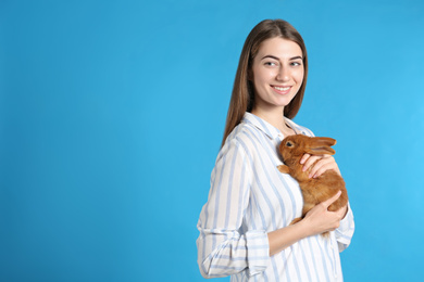 Young woman with adorable rabbit on blue background, space for text. Lovely pet