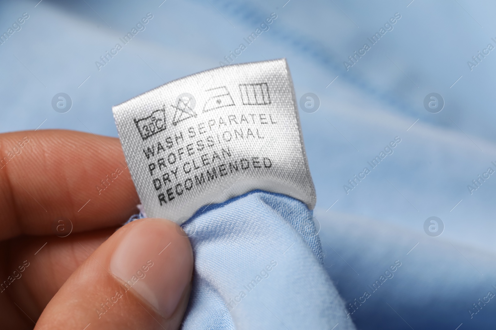 Photo of Woman holding clothing label on light blue garment, closeup
