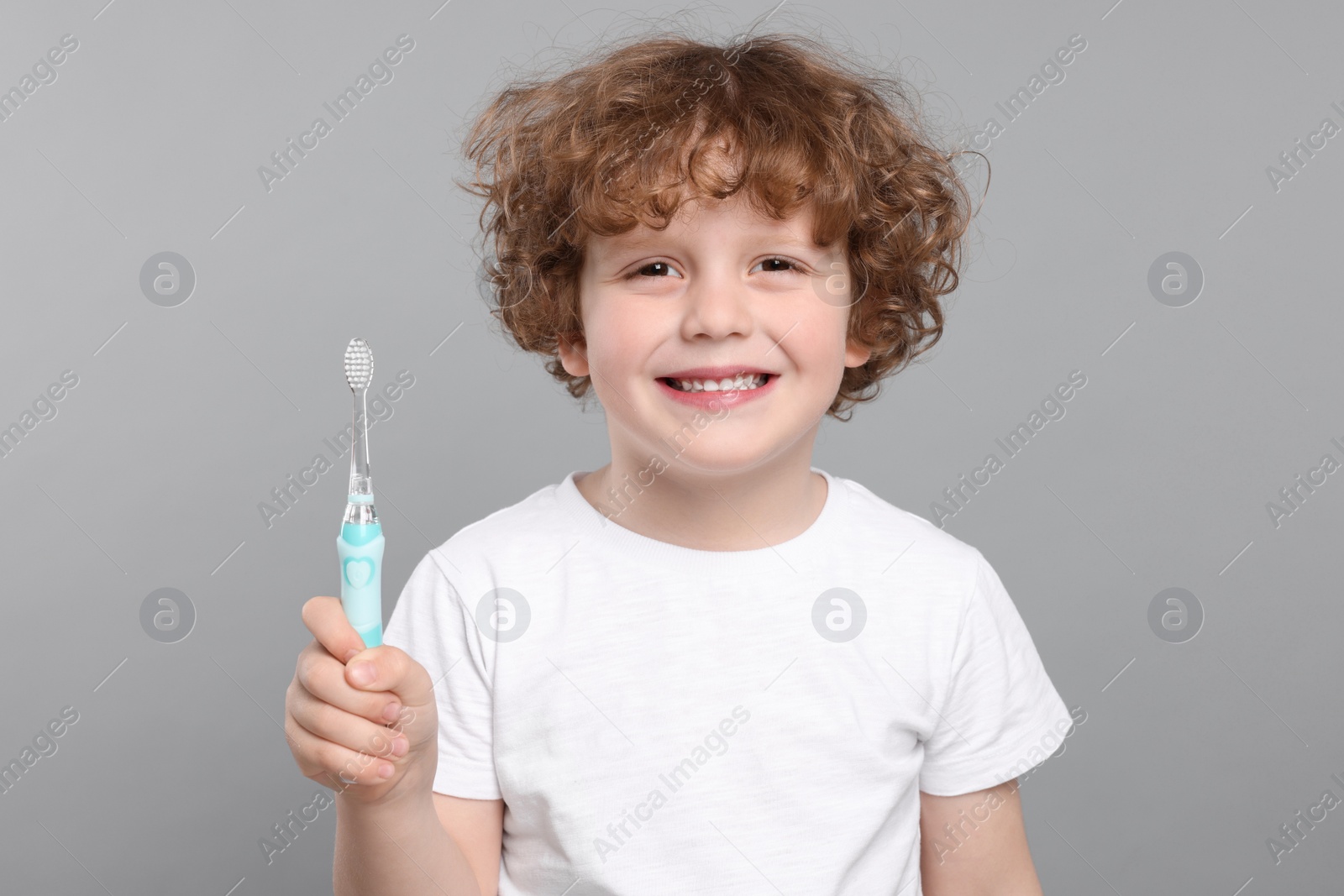 Photo of Cute little boy holding electric toothbrush on light grey background