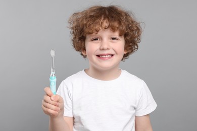Cute little boy holding electric toothbrush on light grey background