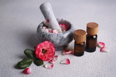 Glass bottles of aromatic essential oil, mortar with roses on white table