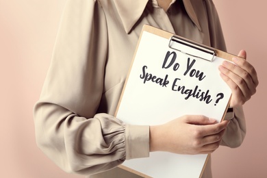 Photo of Woman holding clipboard with question Do You Speak English on pink background, closeup