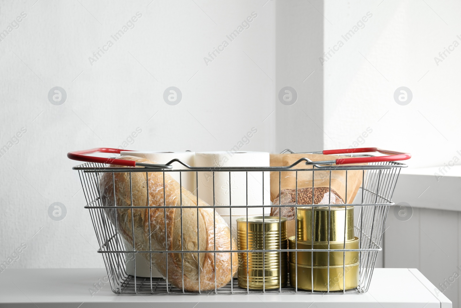 Photo of Shopping basket with products and toilet paper rolls on table indoors. Panic caused by virus