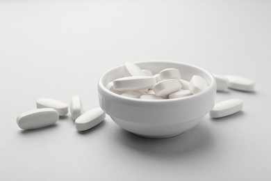 Photo of Vitamin pills in bowl on grey background, closeup