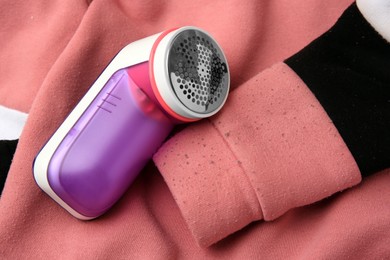 Photo of Modern fabric shaver on colorful sweater with lint, closeup
