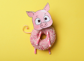 Photo of Funny pig made with donut and piece of paper on yellow background, top view