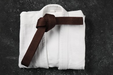 Photo of Brown karate belt and white kimono on gray textured background, top view