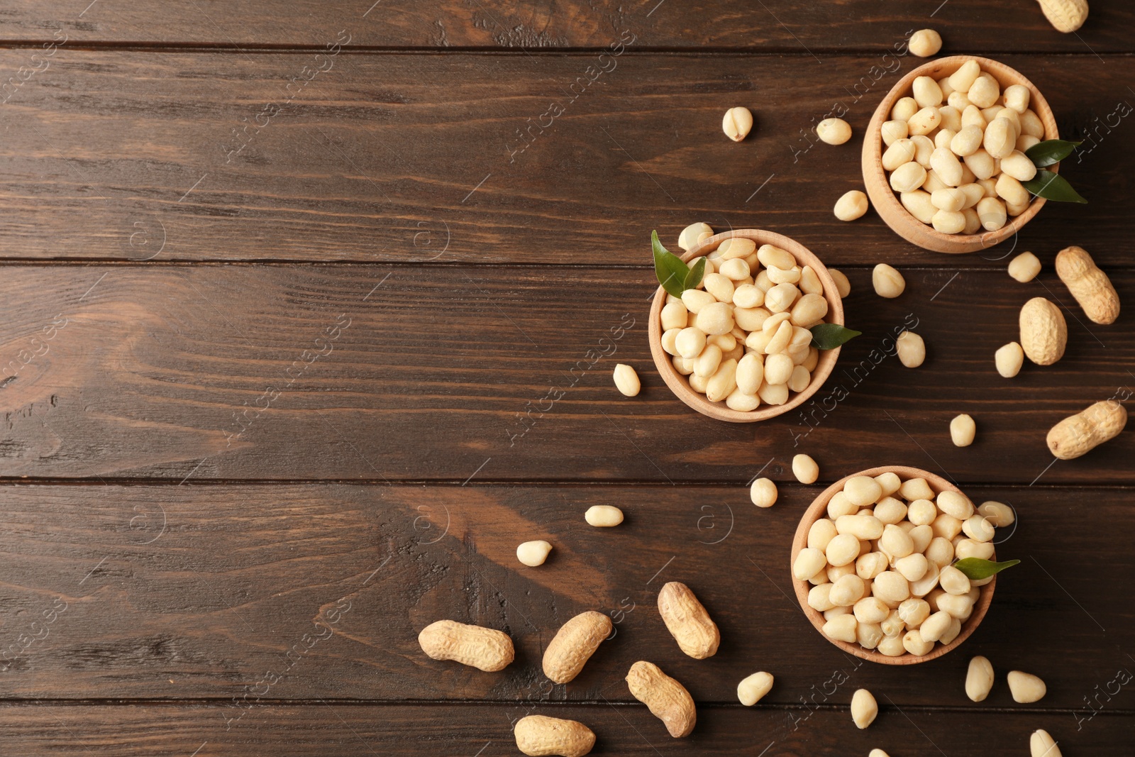 Photo of Shelled peanuts in bowls and space for text on wooden table, top view