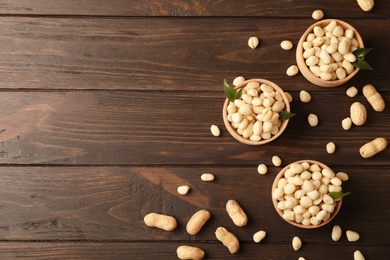 Shelled peanuts in bowls and space for text on wooden table, top view