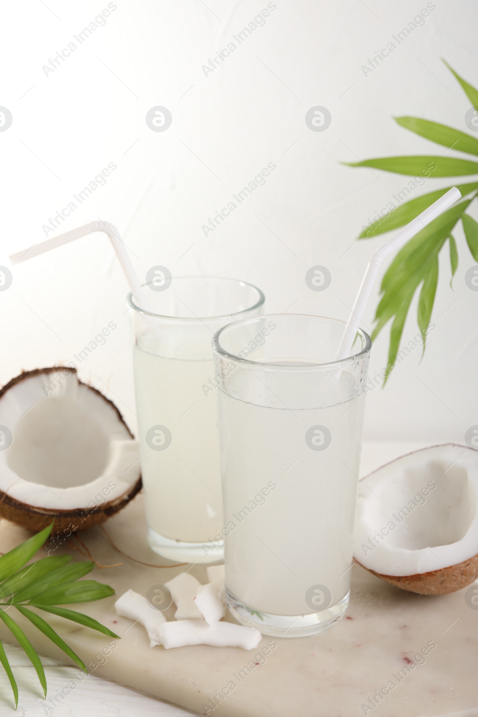 Photo of Glasses of coconut water, palm leaves and nuts on white table