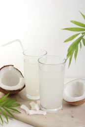 Glasses of coconut water, palm leaves and nuts on white table