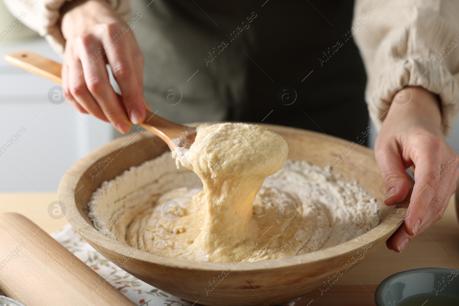 Photo of Woman kneading dough with spoon in bowl at wooden table indoors, closeup