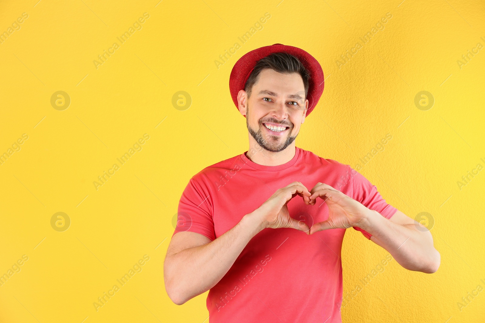 Photo of Portrait of handsome man making heart with his hands on color background, space for text